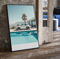 Cream Porsche 911 poolside framed car poster with palms print in a black frame leaning beside a vintage door on parquet