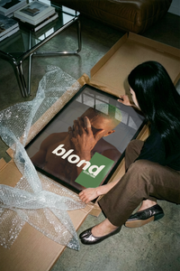 Woman lifting a Frank Ocean Blond wall art print out of a brown cardboard shipping tube
