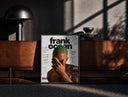 Black-framed Frank Ocean with green hair print on a moody console with designer coffee-table books