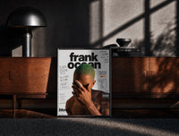 Black-framed Frank Ocean with green hair print on a moody console with designer coffee-table books