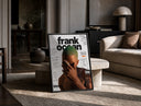 Frank Ocean with green hair print in a black frame leaning on a travertine table in a sunlit lounge