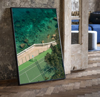 Seaside tennis court by ocean print in a black frame leaning beside a vintage door on parquet