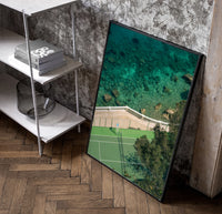 Seaside tennis court by ocean poster in a black frame leaning beside a shelf in a raw-plaster loft