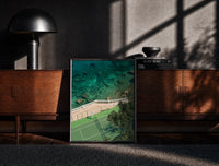 Black-framed Seaside tennis court by ocean print on a moody console with designer coffee-table books