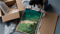 Seaside tennis court by ocean framed print being unpacked from protective bubble wrap and a box