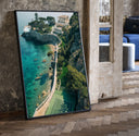 Cliffside coastal luxury villa estate print in a black frame leaning beside a vintage door on parquet