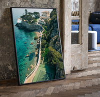 Cliffside coastal luxury villa estate print in a black frame leaning beside a vintage door on parquet