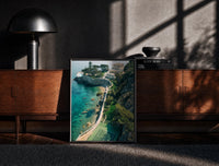 Black-framed Cliffside coastal luxury villa estate print on a moody console with designer coffee-table books