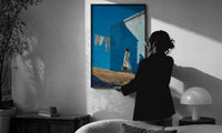 Girl Hanging Laundry in the Sun print in a slim black frame being hung on a sunlit wall in a monochrome room