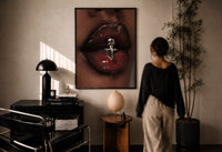 Glossy Lips with a Silver Charm print in a black frame on a sunlit plaster wall, a woman looking on beside a mushroom lamp