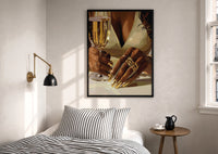 Gold Nails and a Stemmed Glass print in a black frame above a bed with striped linens, a brass wall lamp and a sunlit window