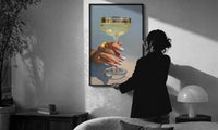 Champagne Coupe print in a slim black frame being hung on a sunlit wall in a monochrome room