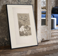 Winged figures and bird-people above sleeping women print in a black frame leaning beside a vintage door on parquet