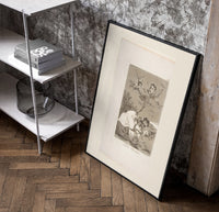 Winged figures and bird-people above sleeping women poster in a black frame leaning beside a shelf in a raw-plaster loft