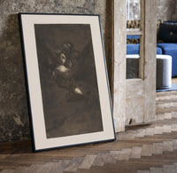 Nightmarish figures with grotesque faces print in a black frame leaning beside a vintage door on parquet