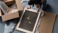 Nightmarish figures with grotesque faces framed print being unpacked from protective bubble wrap and a box
