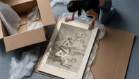 grotesque devils and figures with book framed print being unpacked from protective bubble wrap and a box