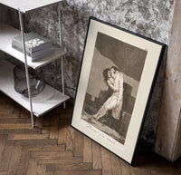 man embracing dying woman poster in a black frame leaning beside a shelf in a raw-plaster loft