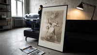 Owl above bound couple print in a slim black frame leaning on a dark sofa in a concrete print studio