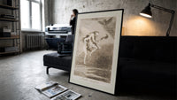 Two witches flying on a broom print in a slim black frame leaning on a dark sofa in a concrete print studio