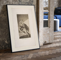 Man with grotesque mask figures print in a black frame leaning beside a vintage door on parquet