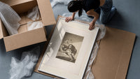 Man with grotesque mask figures framed print being unpacked from protective bubble wrap and a box