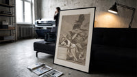 Sleeping man surrounded by owls and bats print in a slim black frame leaning on a dark sofa in a concrete print studio