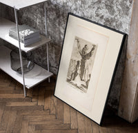 Kneeling woman praying before robed figure poster in a black frame leaning beside a shelf in a raw-plaster loft