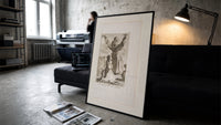 Kneeling woman praying before robed figure print in a slim black frame leaning on a dark sofa in a concrete print studio