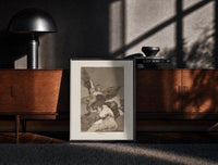 Black-framed Winged demon carrying frightened figure print on a moody console with designer coffee-table books