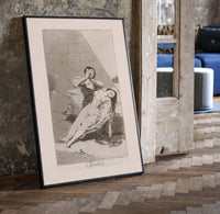 Man grieving over collapsed woman print in a black frame leaning beside a vintage door on parquet