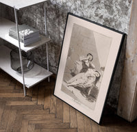 Man grieving over collapsed woman poster in a black frame leaning beside a shelf in a raw-plaster loft