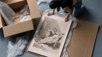 Man grieving over collapsed woman framed print being unpacked from protective bubble wrap and a box