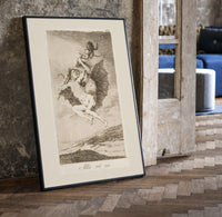 Witches flying with monkey demon print in a black frame leaning beside a vintage door on parquet