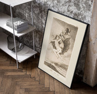Witches flying with monkey demon poster in a black frame leaning beside a shelf in a raw-plaster loft