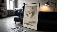 Witches flying with monkey demon print in a slim black frame leaning on a dark sofa in a concrete print studio