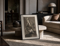 Grotesque figures climbing atop one another print in a black frame leaning on a travertine table in a sunlit lounge
