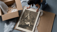 Grotesque figures climbing atop one another framed print being unpacked from protective bubble wrap and a box