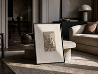 witch scene with goat demon print in a black frame leaning on a travertine table in a sunlit lounge