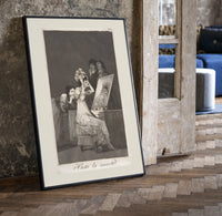 Old woman at vanity mirror print in a black frame leaning beside a vintage door on parquet