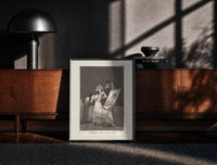 Black-framed Old woman at vanity mirror print on a moody console with designer coffee-table books