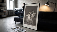 Old woman at vanity mirror print in a slim black frame leaning on a dark sofa in a concrete print studio