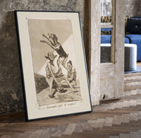 Grotesque demons and goat figure print in a black frame leaning beside a vintage door on parquet