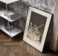 Grotesque nude figures under night sky poster in a black frame leaning beside a shelf in a raw-plaster loft