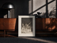 Black-framed Grotesque nude figures under night sky print on a moody console with designer coffee-table books