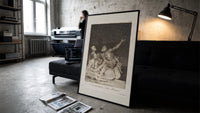 Grotesque nude figures under night sky print in a slim black frame leaning on a dark sofa in a concrete print studio