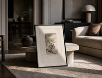 Grotesque figures carrying woman aloft print in a black frame leaning on a travertine table in a sunlit lounge