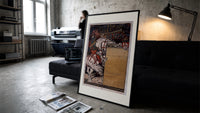 Medieval herald on white horse with trumpet print in a slim black frame leaning on a dark sofa in a concrete print studio