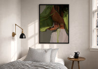 Green Tie-Back Blouse and White Trousers print in a black frame above a bed with striped linens