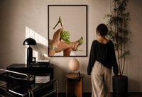 Green Woven Stiletto Sandals print in a black frame on a sunlit plaster wall, a woman looking on beside a mushroom lamp